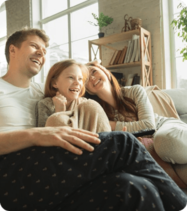 A warm image of a family of three laughing on their sofa with a bookcase in the background